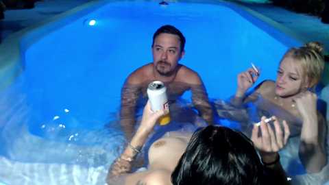 Media: Video of three nude people in a blue-tiled hot tub. A shirtless man with a beard, a blonde woman with a bun, and a brunette woman with wet hair.