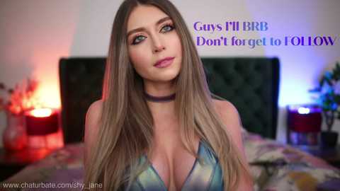 Media: Video of a curvy, light-skinned woman with long, straight blonde hair and blue eyes, wearing a low-cut tie-dye top, standing in a dimly lit bedroom. Text in the background reads, \"Guys I'll BBR Don't forget to FOLLOW.\