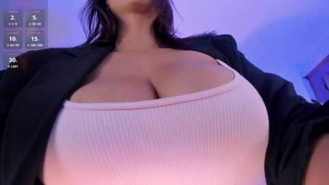 Media: Video of a woman with large breasts in a low-cut white tank top, partially covered by a black blazer, taken from a low angle, showing ample cleavage.