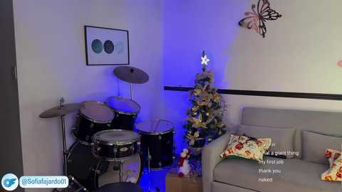 Media: A video of a cozy, modern living room with a festive Christmas tree, a drum set, and a grey sofa adorned with holiday-themed pillows.