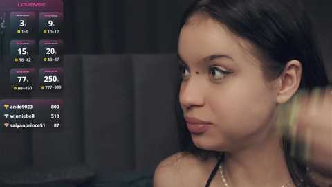 Media: A video of a young, fair-skinned woman with long dark hair, wearing a pink top, looking introspectively. The background features a dark, blurry setting and a digital overlay showing social media activity.