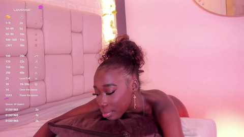 Media: Video of a topless, dark-skinned woman with curly hair in a bun, lying on a bed, surrounded by pink lighting, with a text overlay showing her stats.