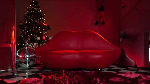 Media: Video of a red, inflatable heart-shaped couch with a red light glow, a lit Christmas tree adorned with ornaments, and a checkered floor, creating a festive, romantic, and whimsical ambiance.