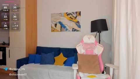 Media: Video of a modern, minimalistic living room with a blue sofa, yellow star pillow, white chair with pink cushion, and abstract art on a white wall.