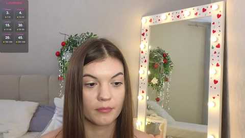 Media: Video of a young woman with straight brown hair, light skin, and no makeup, standing in front of a mirror with red heart decorations and a countdown timer on the wall.