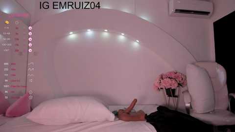 Media: Video of a minimalist, pink-themed bedroom with a white, curved headboard, string lights, and a white air conditioner. A partially visible person lies on the bed, holding a dog.