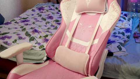 Media: Video of a pink gaming chair with white accents and floral-patterned bedding in a cozy bedroom.