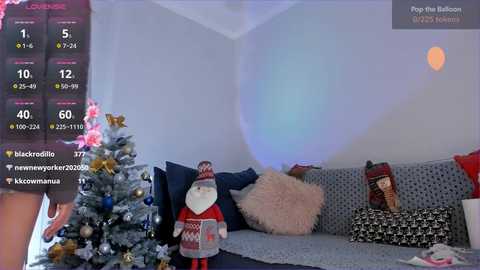 Media: Video of a cozy living room with a Christmas tree, a plush Santa, and patterned pillows on a gray sofa.