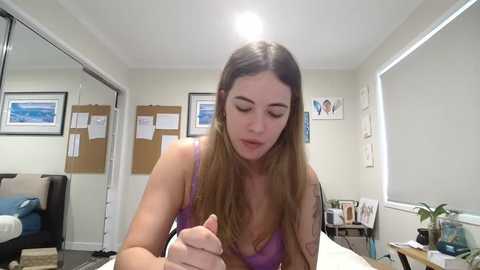 Media: A video of a young woman with long, brown hair in a lavender tank top, sitting at a desk in a brightly lit, modern office.