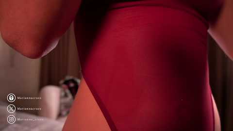 Media: Close-up video of a woman wearing a sheer, red, high-cut bodysuit, showcasing her toned thighs and buttocks. The background features a dimly lit bedroom with blurred furniture, emphasizing the intimate, sensual nature of the scene.