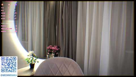 Media: Video of a modern room with soft, flowing white and gray curtains. A round, white, quilted chair is positioned in the foreground. A vase of pink flowers sits on a white table. Social media icons and a QR code are visible in the upper left corner.