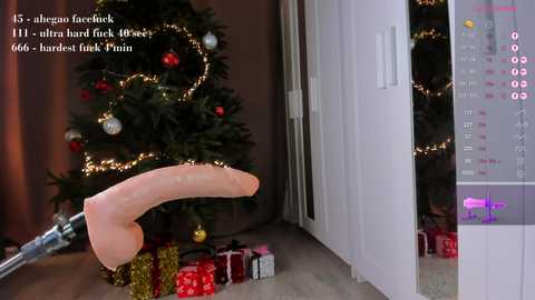 Media: A video showing a realistic, erect, uncircumcised, light-skinned penis with a curved shaft, placed near a decorated Christmas tree. The background includes a modern room with white walls and a white cabinet.