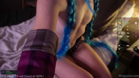 Media: A blurry, low-resolution screenshot from a live stream shows a woman with long, blue braided hair wearing a purple and black plaid skirt, lying on a bed with dim lighting.