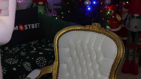 Media: Video of a vintage, gold-framed, tufted chair with white upholstery, set against a festive, dimly lit background featuring a decorated Christmas tree, colorful lights, and Christmas-themed decorations.