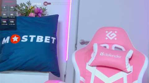 Video of a pink gaming chair with a white emblem on a white wall, next to a blue pillow with \"MOSTBET\" and a star logo.