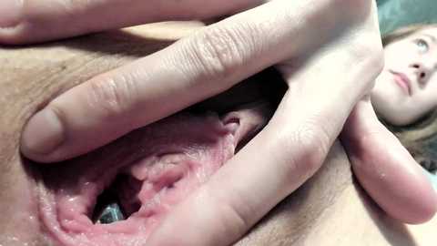 Media: Video of a woman's vulva being spread apart by her fingers, showing detailed inner anatomy, with a partially visible face in the background.