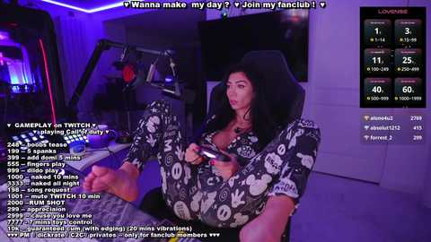 Media: Video of a woman in black patterned pajamas, sitting on a gaming chair, playing a video game, with a Twitch overlay showing chat messages.