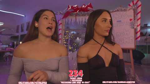 Media: Video of two women in a festive setting, one in a grey off-shoulder top, the other in a black halter dress, surrounded by Christmas decorations and a chalkboard sign.