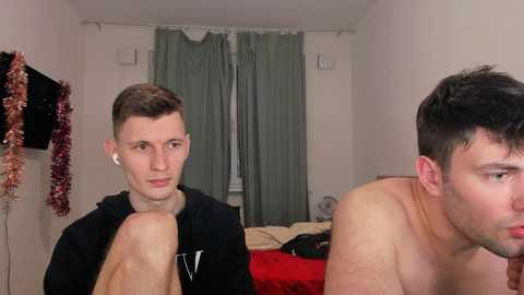 Media: A video of two shirtless men in a simple room. One is focused, wearing a black hoodie, while the other appears to be in thought.