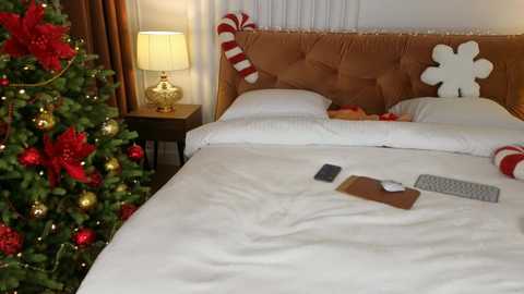 Media: Video of a cozy, festive hotel room with a Christmas tree, a bed with white linens, a laptop, and holiday decorations.