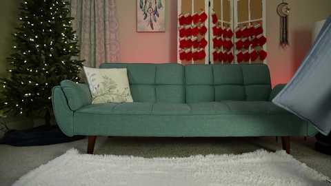 Media: Video of a teal mid-century modern sofa with a cream pillow, adorned with Christmas decorations including a tree, red stockings, and a wreath, set against a softly lit, cozy room with a fluffy white rug.