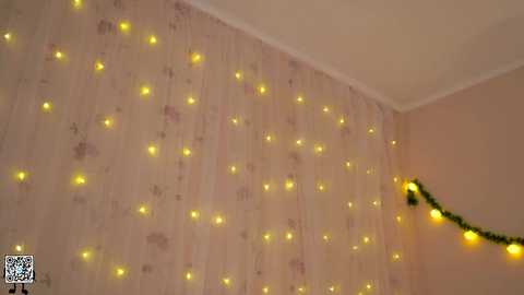 Media: Video of a cozy room with a beige wall adorned with a string of warm, yellow fairy lights, creating a festive ambiance. A garland with green lights hangs from the corner.