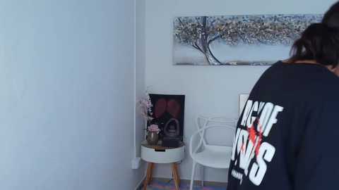 Media: A video of a minimalist room with a white wall and a large framed tree painting. A person with a black hoodie and the word \"LOVE\" on it stands in the foreground.