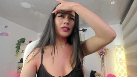 Media: A video of a Latina woman with long black hair, wearing a black lace bralette, wiping sweat from her forehead. She's indoors, in a brightly lit room with white walls and a floral arrangement.