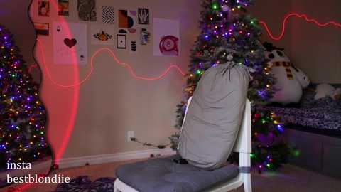 Media: Video of a cozy bedroom with a Christmas tree adorned with colorful lights, a gray cushioned chair, and festive decorations on the beige wall.