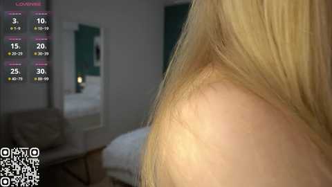 Media: Video of a woman's bare shoulder with long blonde hair, taken from behind. The background shows a dimly lit bedroom with a bed, a wall-mounted clock, and a QR code at the bottom.