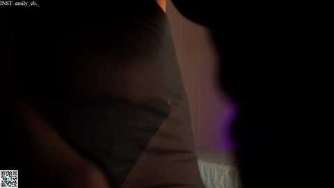 Media: A dimly lit video of a person's back, partially obscured by a dark figure, with a faint, glowing purple light in the background. The scene is dark and atmospheric.