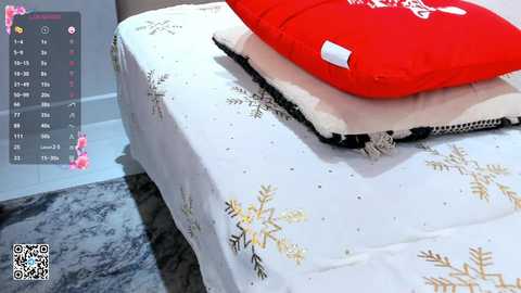 Media: Video of a neatly made bed with a white duvet adorned with gold snowflake patterns and a red pillow. A fluffy white blanket is folded at the foot. A calendar with pink flowers and a dog is visible in the background.