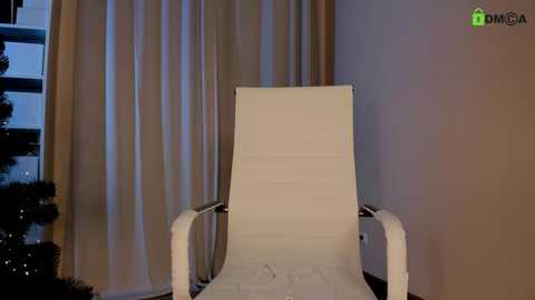 Video of a white, modern recliner chair with armrests, placed against beige curtains in a dimly lit room, with a green \"DMCA\" watermark in the top right corner.