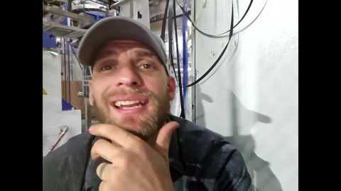 Media: A video of a bearded, smiling man in a white cap and dark jacket, giving a thumbs-up in a cluttered industrial room with wires and machinery in the background.