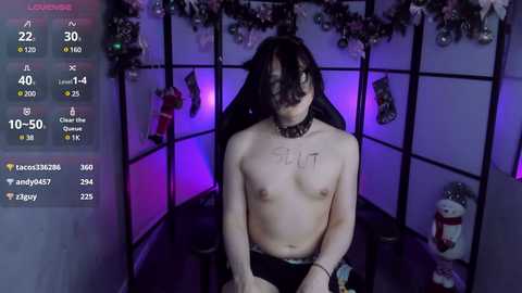 Media: A video of a topless, androgynous person with long, dark hair, wearing a spiked collar, sitting in a dark room adorned with Christmas decorations and purple lighting. Text overlays show chatroom messages.