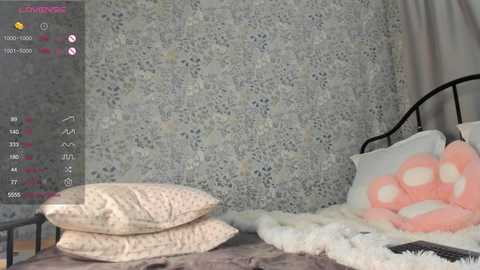 Media: Video of a cozy bedroom with a white, textured blanket, light-colored pillows, and a soft, fluffy white rug. A black metal bed frame holds plush toys, including a large pink bear. The background features intricate, floral wallpaper.