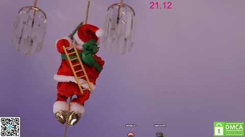 Video of a Santa Claus figurine hanging from a rope in a room with a purple background. The figurine is dressed in a red suit, green belt, and gold boots, with a ladder attached.