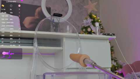 Media: Video of a modern living room with a white cabinet, a glowing star tree, and a clear tube connected to a wooden hand pump, displaying a live stream.