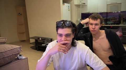 Media: Video of two young, shirtless, Caucasian men in a modern living room; one with goggles on head, the other with hand in mouth.