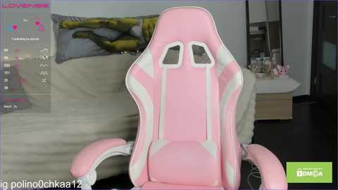 Video of a pink and white gaming chair with a cushioned seat and backrest, placed in a modern living room with a beige couch and colorful pillow.