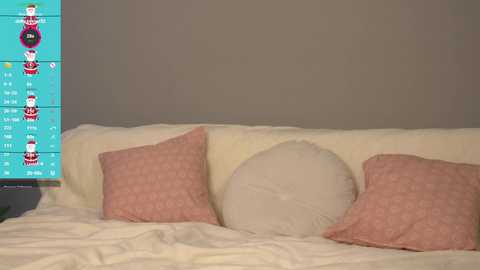 Media: A video of a cozy bedroom with a cream-colored bed, two pink-patterned pillows, and a white pillow, set against a muted gray wall. A colorful, digital calendar with cartoon characters is partially visible on the left.