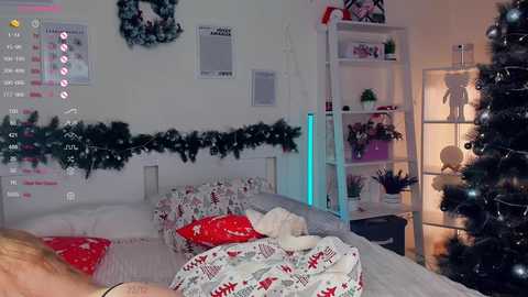 Media: Video of a cozy, festive bedroom with a Christmas tree, a white bed adorned with red and white bedding, and a white bookshelf decorated with holiday ornaments.