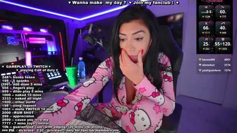 Media: A video of an Asian woman in a pink Hello Kitty pajama set, seated in a dimly lit room with neon lighting, engaging in a live stream on Twitch.