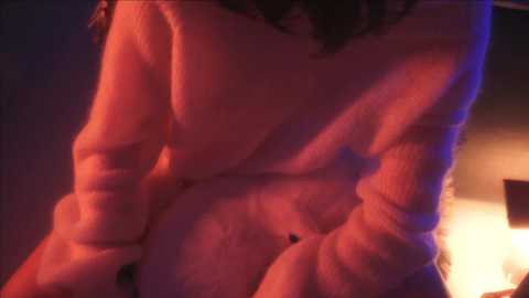 Media: Video of a person wearing a cream-colored sweater, with a partially visible tattoo on the right arm. Background features dim lighting and warm tones.