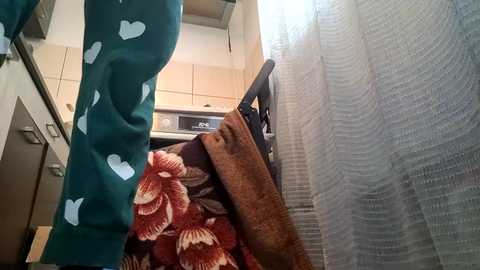 Media: Video of a person in teal pajamas with white heart patterns, holding a smartphone, in a modern kitchen with white cabinets and a window with sheer white curtains.