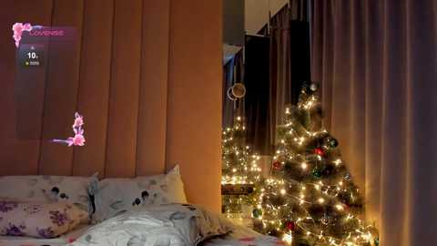 Media: Video of a cozy bedroom with a lit Christmas tree near a bed adorned with festive bedding, featuring a pink and purple floral pattern.