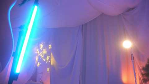 Media: Video of a dimly lit, purple-hued tent with white fabric walls, featuring a glowing blue LED light and a warm yellow lamp, creating a mystical, dreamlike atmosphere.