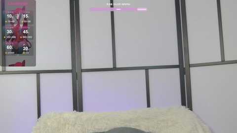 Video of a modern, minimalist room with white walls and a gray grid pattern. A white fluffy rug is visible in the foreground. A weather display and a pink progress bar are visible on the wall.