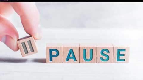 Media: Video of a hand holding a wooden block with \"PAUSE\" in blue letters, placed on a white surface. The background is blurred, emphasizing the block's minimalist design.