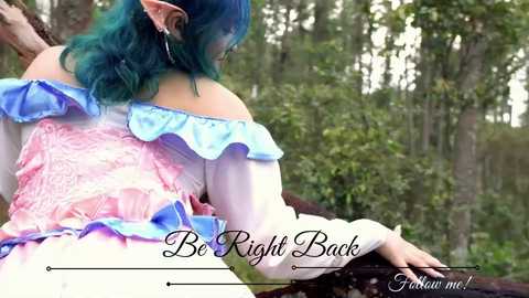 Media: Video of a person with teal hair, wearing a pink and blue off-shoulder dress, standing on a wooden porch. The background features a dense forest. Text reads \"Be Right Back\" and \"Follow me!\